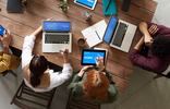Team werkt samen aan laptops en tablets rond een tafel.